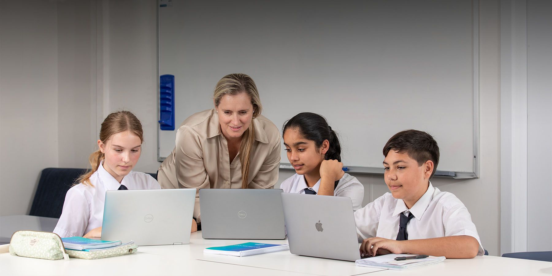 Middle School teacher assisting students on laptops