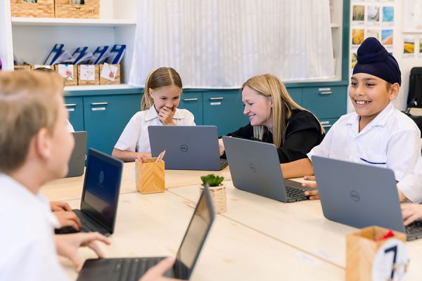 Junior School teacher helping students on their laptop